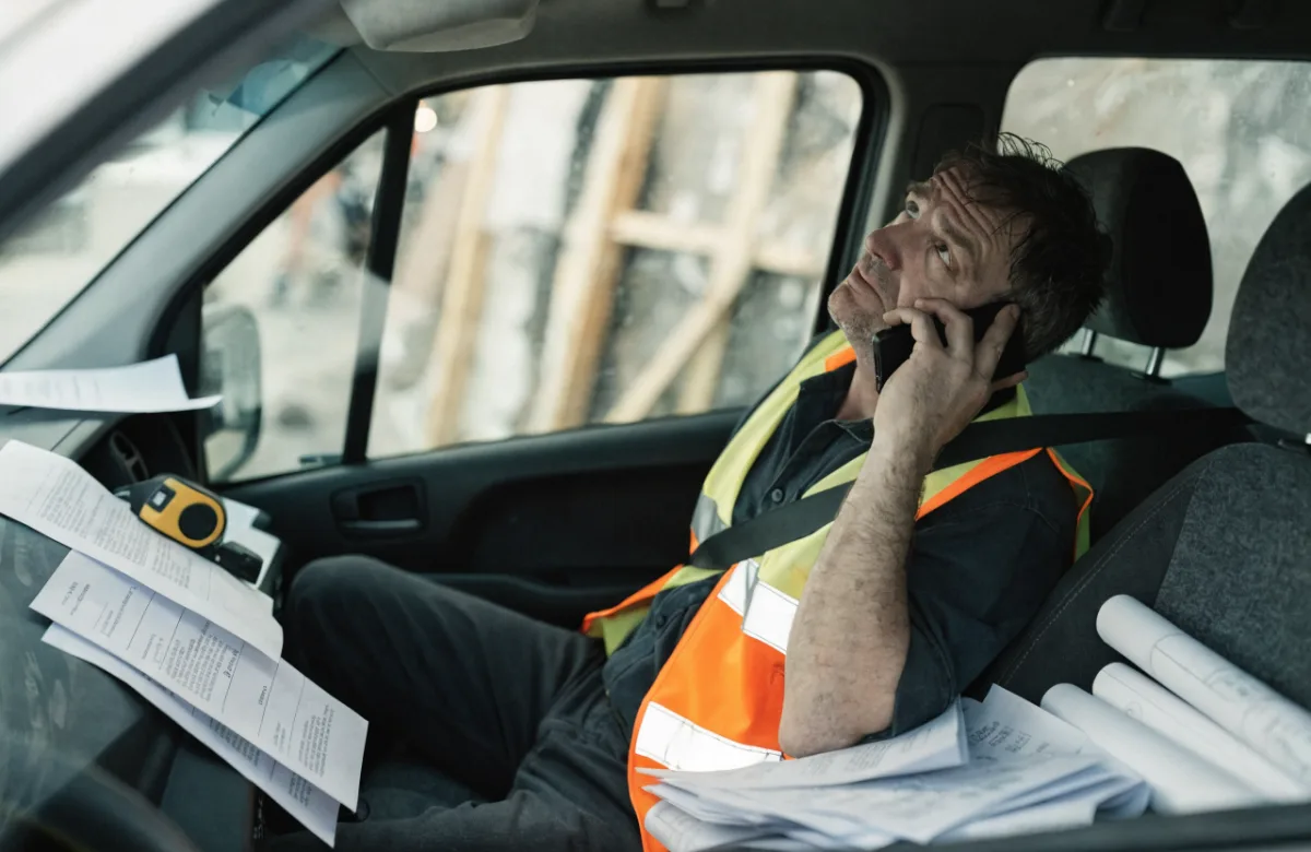 Aannemer met verspreide administratie, papierwerk en telefoon